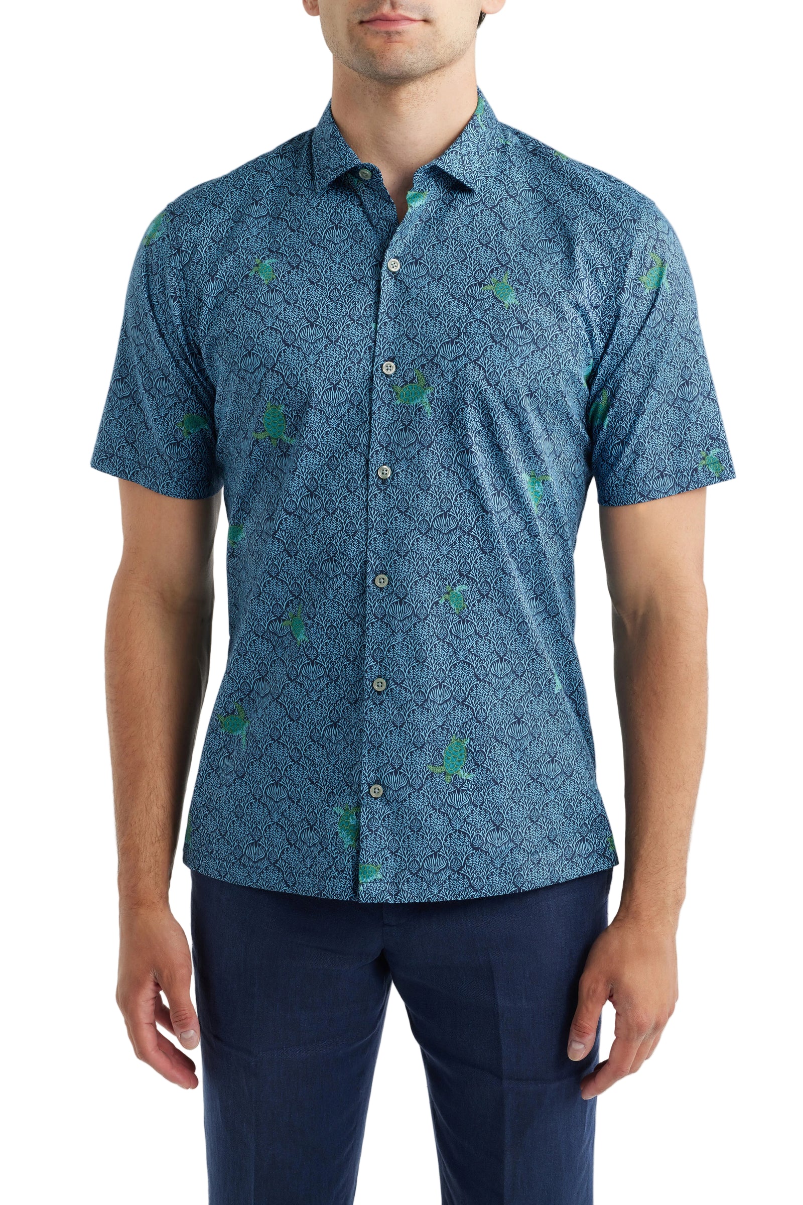 A man wearing a short-sleeve button-up shirt with a blue and green geometric pattern, paired with navy trousers, against a light gray studio background.